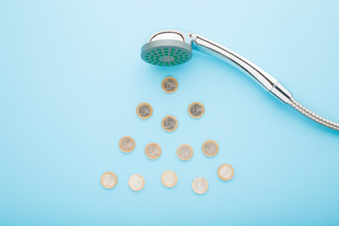 Euro coins as drops falling from shower head on light blue table background. Blue pastel colour background. Closeup. Water consumption and saving concept.