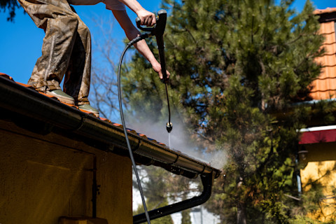 A person cleaning roof tiles using a power washer