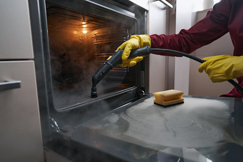 A professional oven cleaner is using a specialised tool to deep clean an oven.