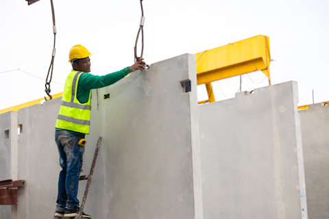 This image shows a construction worker standing on reinforced concrete structures at a building site, wearing safety gear and surrounded by industrial equipment.