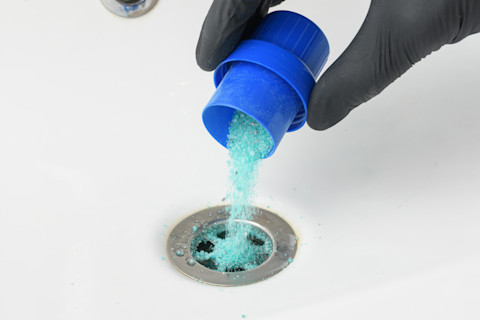 A man is pouring some solution down a drain to clean it