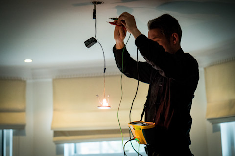 An electrician standing on a stool and fixing lights on the ceiling.