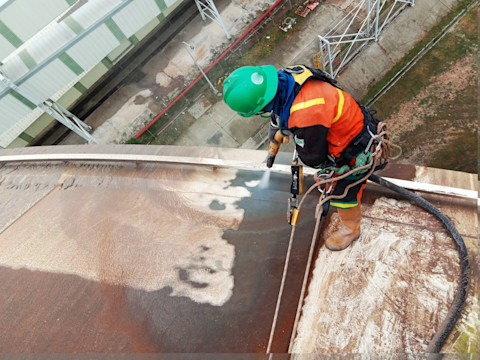 A painter with a green cap sandblasting to remove paint.