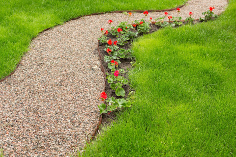 This image shows a garden path made of small gravel, bordered by neatly trimmed grass and flowers, creating a tidy and inviting walkway.