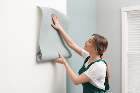 Girl hangs wallpaper on a wall.