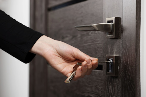 A female hand putting a key in a lock of a black door
