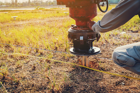 technician installing ground screw for mounting structure of solar panel at solar farm
