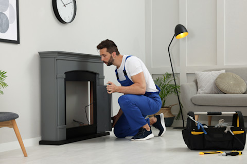A professional installing an electric fire unit on a wall, with tools and equipment nearby, and a partially finished setup featuring the electric fire's sleek design.