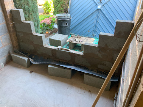 This image shows the process of a garage door being bricked up. The original blue garage door has been removed and is in the background. Breeze blocks have been cemented on top of each other to fill in the gap where the door used to be.