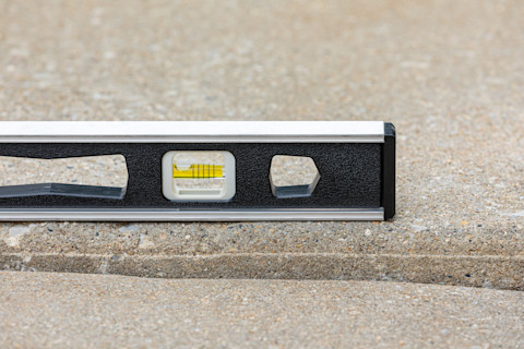 The image shows a close-up of a spirit level placed on a rough concrete surface.
