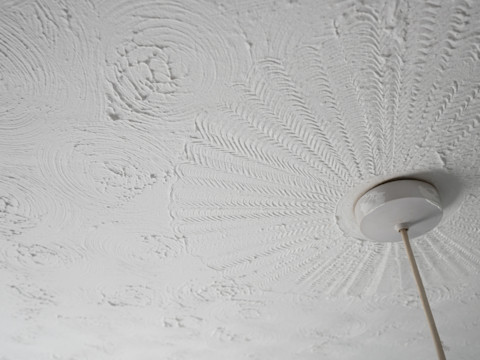 Close-up of a white textured ceiling with circular patterns. A ceiling light fixture is visible, with wires extending downward.