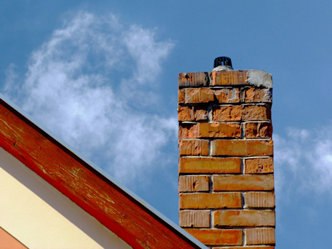 Isolated damaged clay brick chimney with weathered and spalling surface. wood trim on house gable end wall
