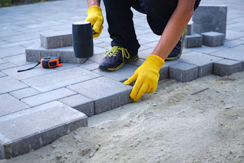 A person wearing yellow gloves lays concrete pavers