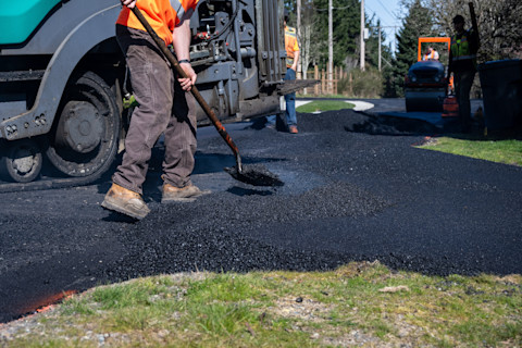 Workers repaving a residential driveway with fresh asphalt.