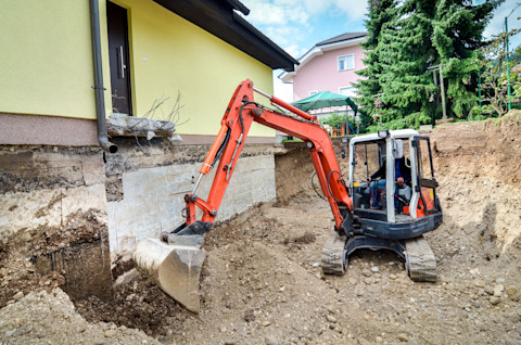 Large family house under renovation with a small digger digging new foundations, showing a renovation in progress.