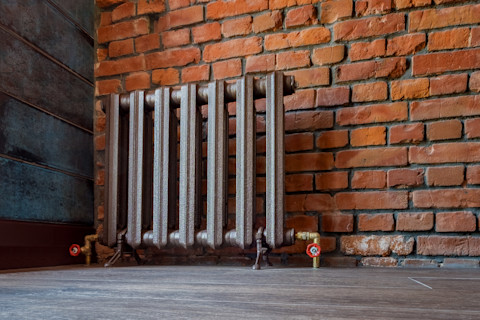 A small vintage style iron radiator against an interior brick wall 