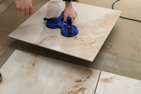 This image shows a close up of a professional tiler laying ceramic tiles on the ground in a bathroom or kitchen.
