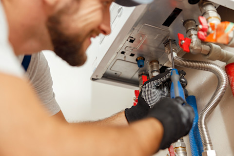 This image shows a plumber using a screwdriver to install a modern boiler unit in a residential setting.