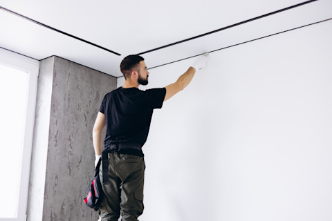 A builder standing on a tool with black t-shirt suspending the ceiling. 