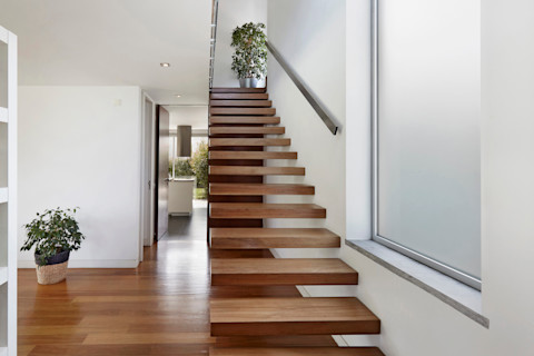 This image shows a staircase with wooden floating stairs and wooden flooring in a mid-brown tone. There are two plants in the midground of the image.