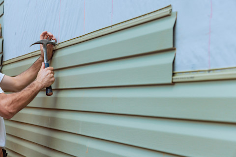 This image shows a tradesperson fitting horizontal planks of cladding to a house with a hammer and nail.