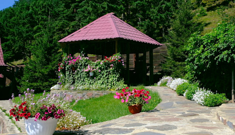 Landscaped garden with a terrace, wooden gazebo, and summer flowers.