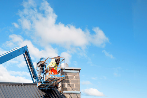Construction workers operating from a telescopic boom lift while installing insulated panels on the facade of a multistory building.


