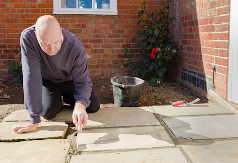  This image shows a builder using a trowel to lay grouting in between patio slabs.
