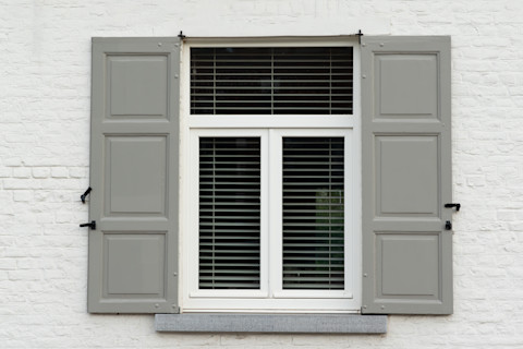 This image shows a window with a white frame with open grey external shutters.