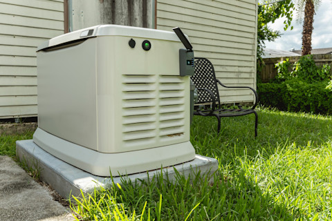 A white colour home generator in a garden next to a black chair.