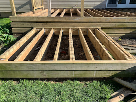This image shows decking in the construction or deconstruction process. The frame is in place but the boards are missing. The decking frame is on top of soil.