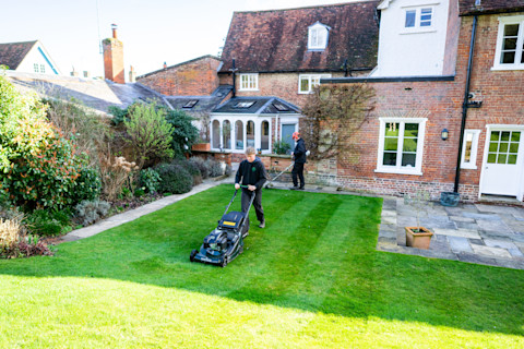A professional lawn care worker using a push lawnmower to cut grass on a well-maintained lawn.