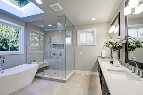 A spacious bathroom in grey tones featuring a freestanding bathtub and a sleek glass-enclosed shower creating a luxurious and contemporary design.
