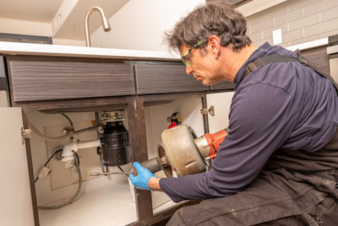 A plumber repairing a garbage disposal.
