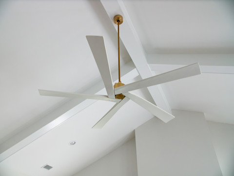 This image shows a modern ceiling fan with thin white blades and a brushed gold downrod.