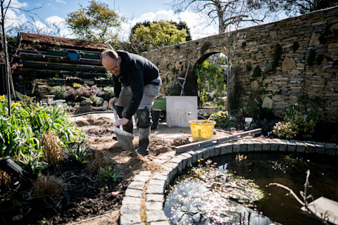 A landscaper fixing a pond with a shovel and other tools.