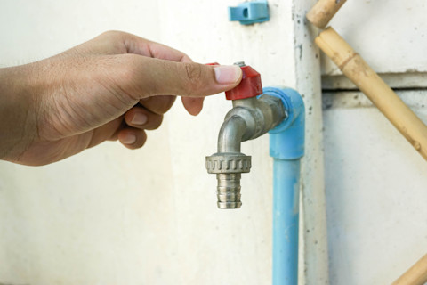 Close-up of an outdoor tap mounted on a wall. The tap is sleek and modern, with a hose connected.