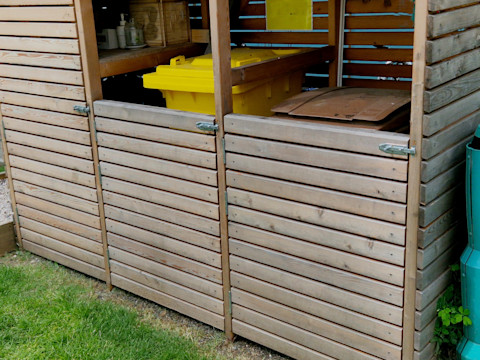 A large wooden bin storage shed with one yellow wheelie bin and one brown one inside it