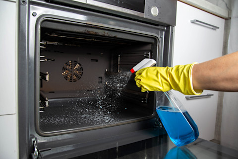 A cleaner with a spray bottle cleaning a oven.