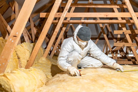 A man in white protective clothes laying loft insulation