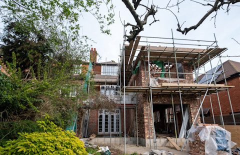 A house extension renovation underway, featuring a three storey brick house with scaffolding around the ongoing extension construction. 