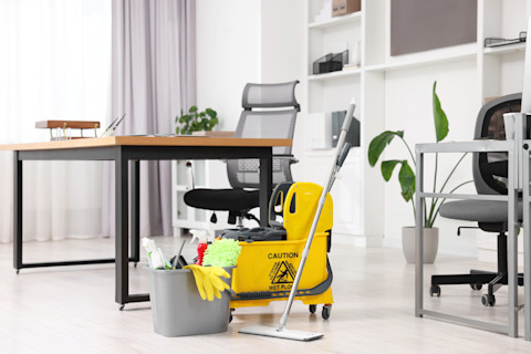 An office set-up with a chair, table, plant and a bucket with cleaning supplies to clean the office.