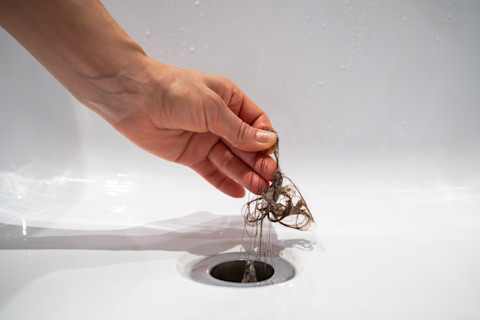 Water drain hole clogged with hair clump. Close up. Cleaning shower polluted sewer system.