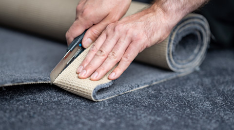 A hand cuts a piece of carpet.