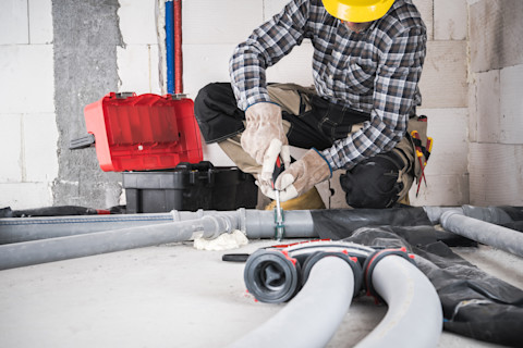A man wearing a helmet is cutting pipes in half on the ground.