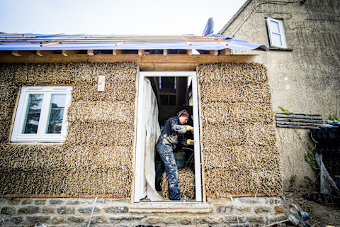 A builder building a straw bale house with white windows.