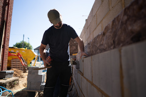 A retaining wall being installed, with workers placing and securing large stone or block segments, and machinery or tools in the background.