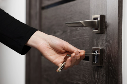 A female hand putting a key in a lock of a black door