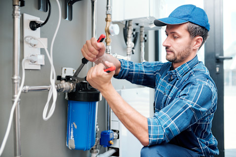 A whole house water filtration system installed in a utility room, showing multiple filter units connected to the main water supply. The image illustrates a typical setup of a water filter system, highlighting components like sediment and carbon filters, pipes, and valves, which influence the overall cost