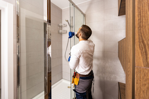 A man installs a shower enclosure in a bathroom.